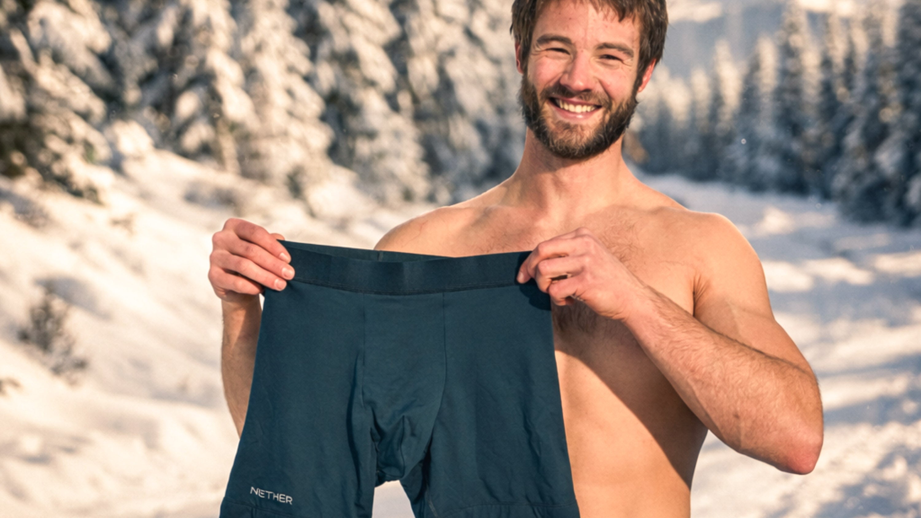 Man smiling while holding Nether Boxer Brief in snowy mountain setting

