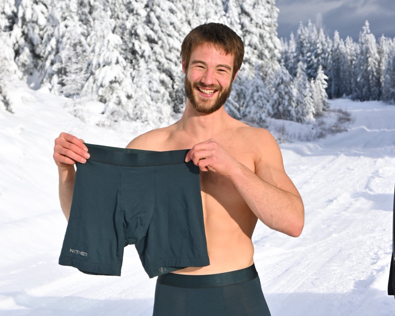 Man holding a pair of dark green boxer briefs in a snowy landscape